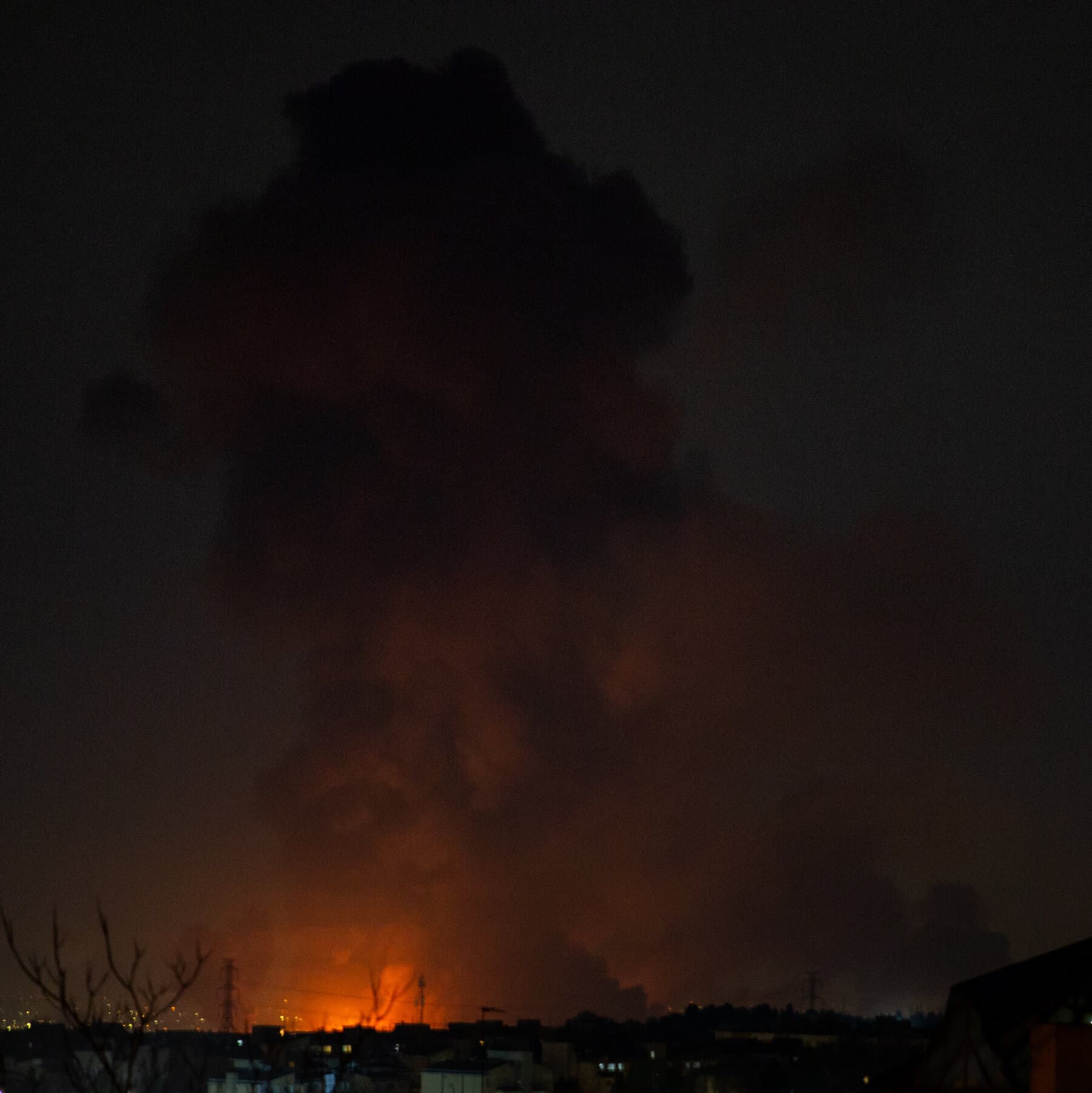 A gritty, cynical political cartoon style image showing a large wooden crate labeled '20,000 BOMBS' being stamped with a giant red stamp that says 'EMERGENCY'. The person holding the stamp is a faceless bureaucrat in a suit. In the background, a small, useless building labeled 'Congress' is covered in cobwebs and ignored. The colors should be muted grays and browns with the bright red of the stamp standing out.