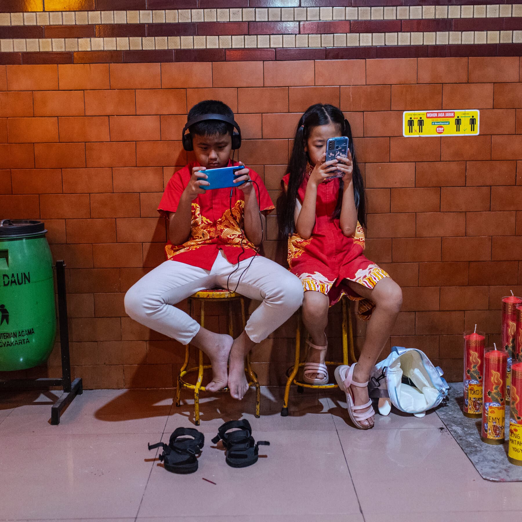 A moody, realistic image of a bored teenager sitting on a curb holding a smartphone. The screen displays a large red 'BLOCKED' icon. In the background, out of focus, a generic government official in a suit stands looking confused and holding a piece of paper. Dark, urban lighting.
