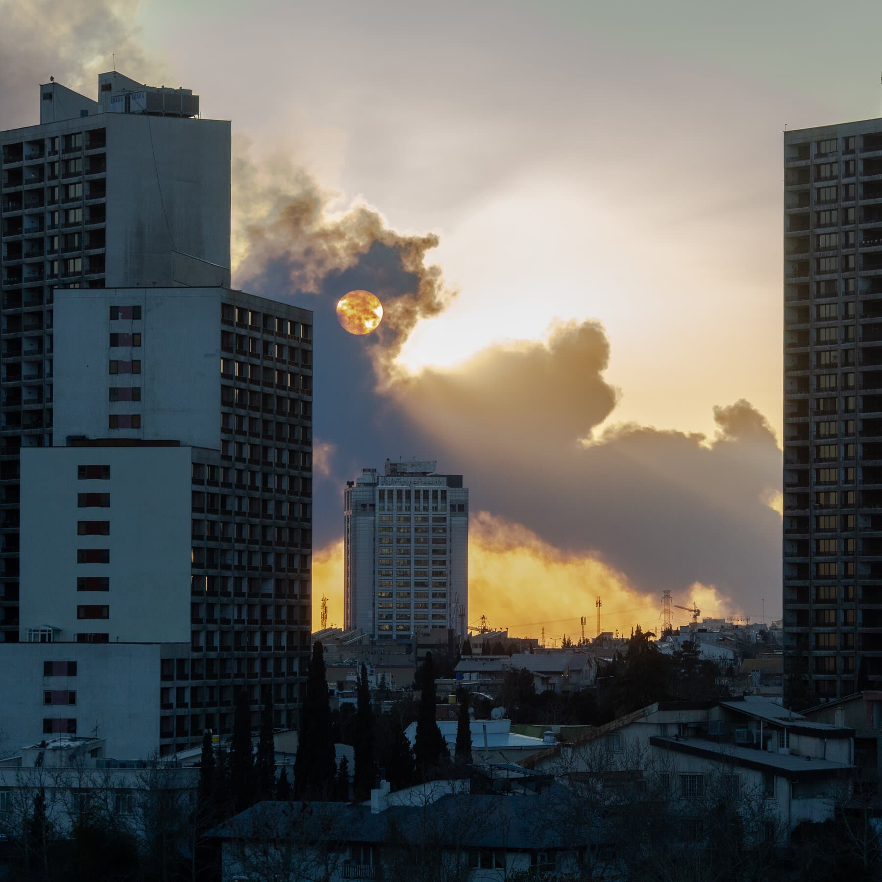 A satirical, high-contrast illustration of a chaotic war room. In the center, a large table is covered in conflicting maps, toy soldiers, and a spilled fast-food drink. A suit jacket hangs on a chair, but the chair is empty. Outside a large window in the background, stylized smoke rises in the distance. The lighting is dim and moody, emphasizing a feeling of abandonment and confusion.