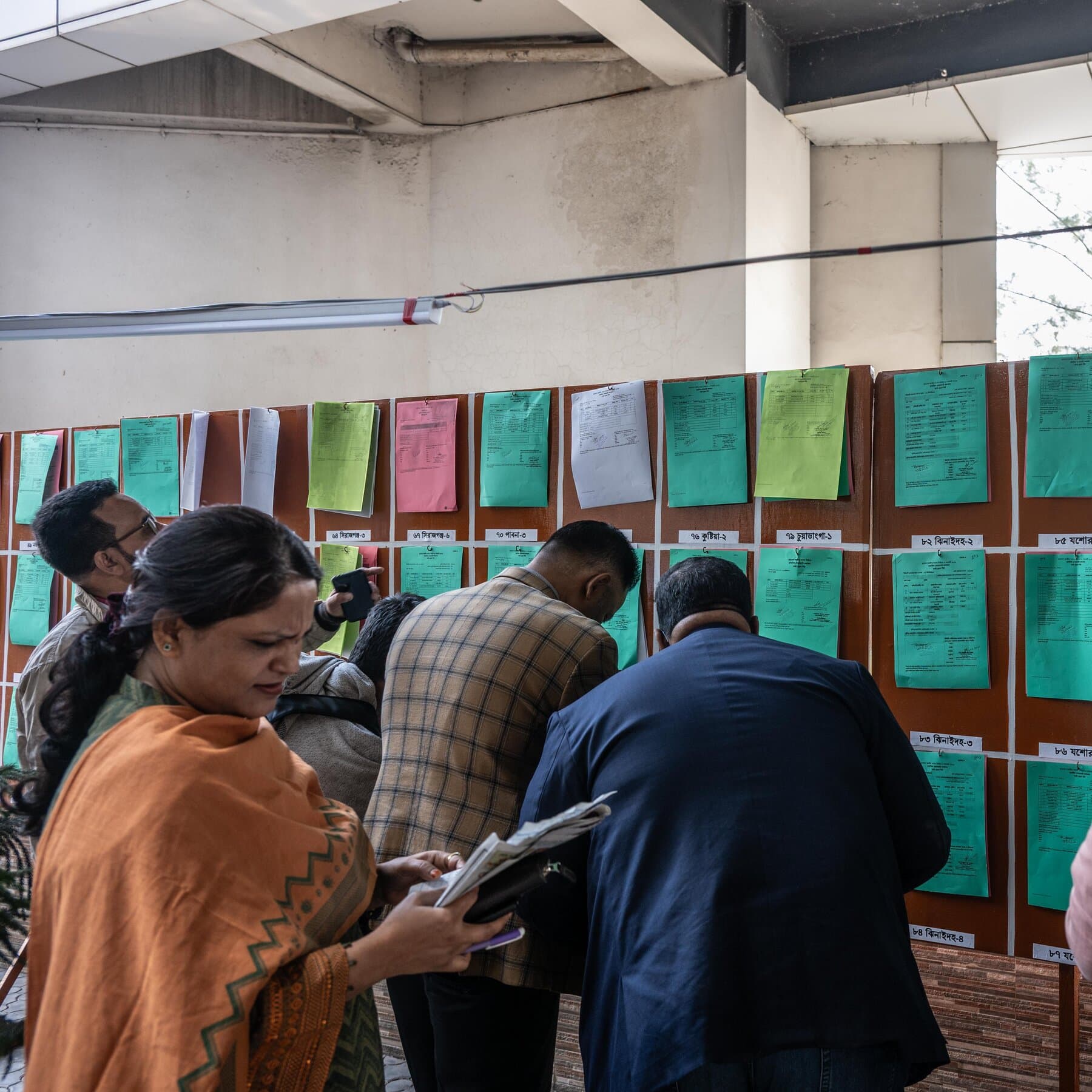 A single, worn-out paper ballot box sitting alone in the middle of a chaotic, dusty street in Dhaka. The box is overflowing with papers that are turning into smoke as they touch the air. The background is a blur of busy crowds and faded political posters on brick walls. Realistic, gritty, high contrast style.